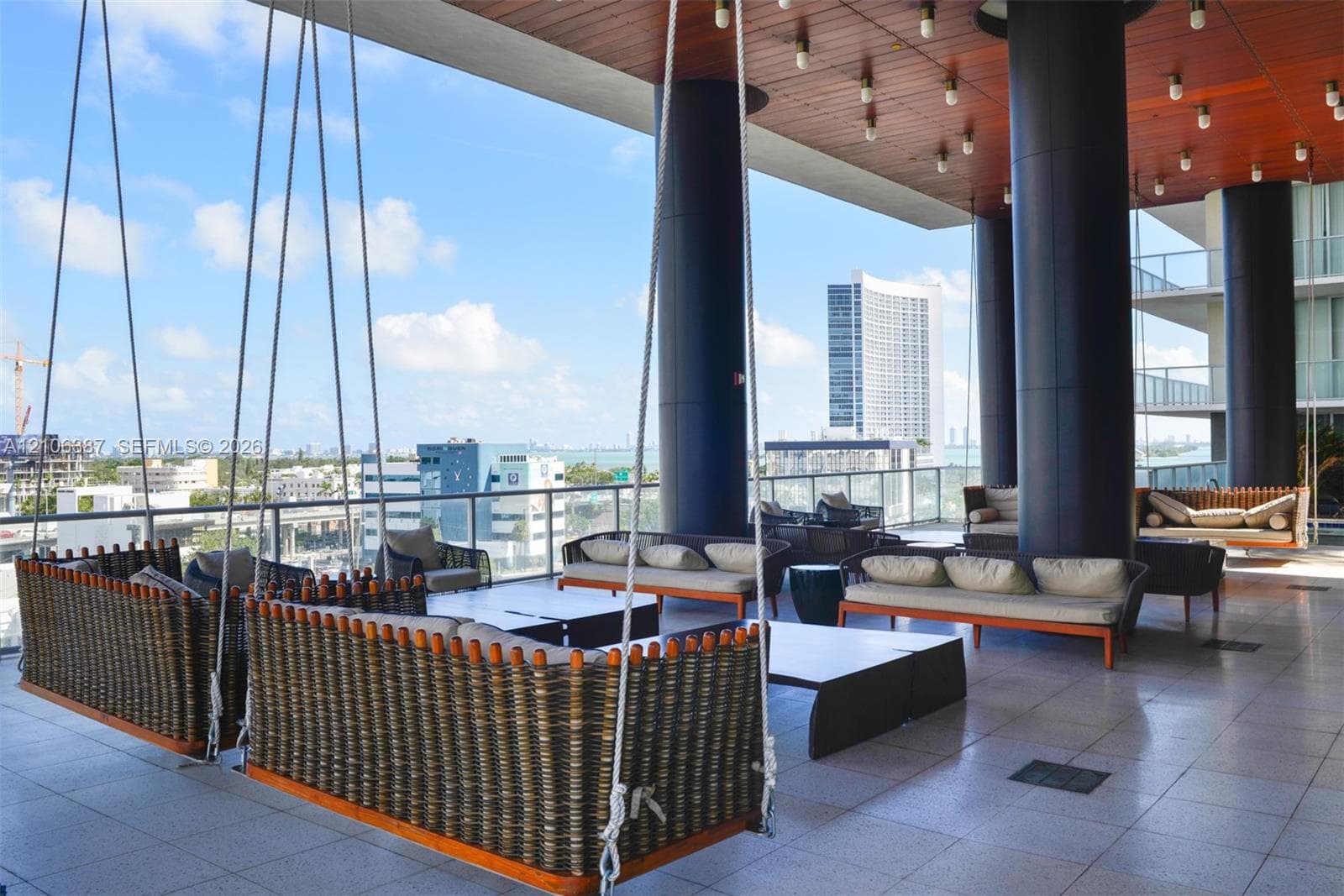 Expansive covered terrace featuring large-format tile flooring, wood-paneled ceiling, recessed lighting, and structural columns with a glass panel railing
