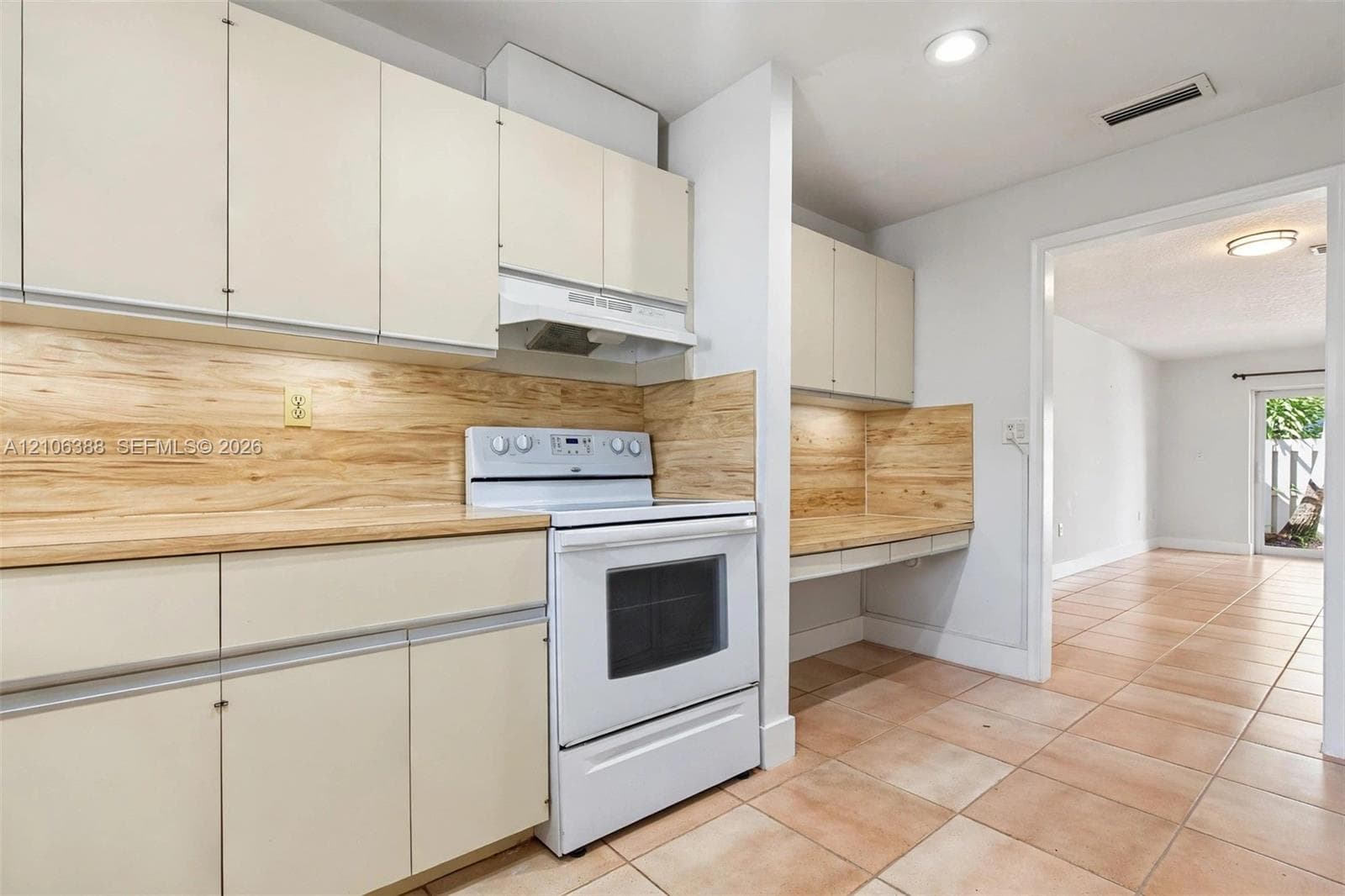 Kitchen featuring flat-panel cabinetry, light-toned wood-finish backsplash, integrated range hood, tile flooring, and built-in workstation