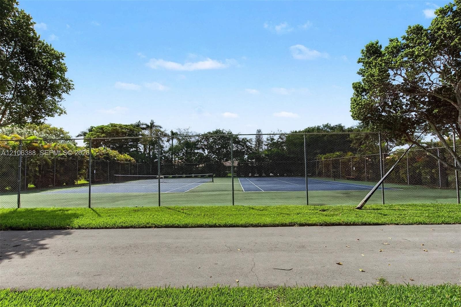 Tennis court featuring a paved surface, chain-link perimeter fencing, and mature surrounding trees