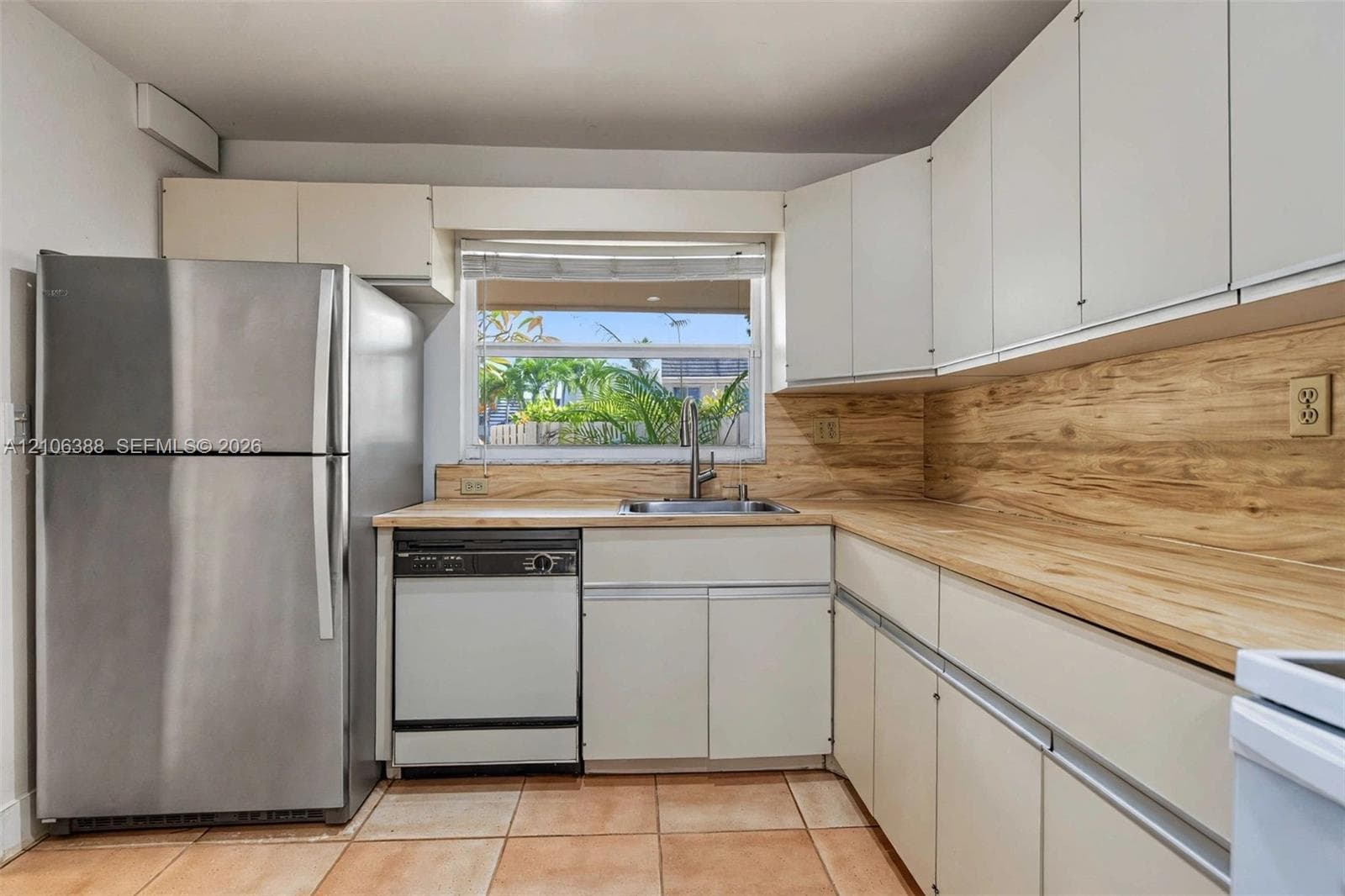 Kitchen featuring flat-panel cabinetry, light wood-finish countertops with matching backsplash, stainless steel refrigerator, stainless steel dishwasher, and ceramic tile flooring