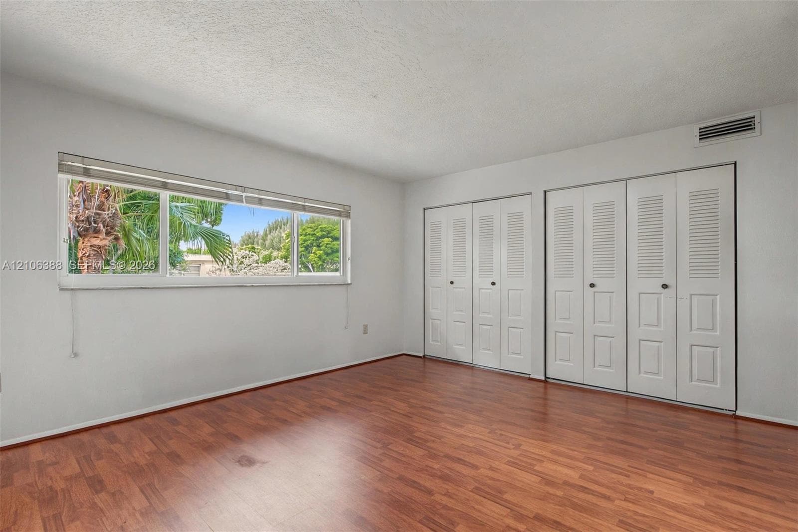 Room featuring wood-finish flooring, large horizontal window, and dual sets of white louvered-panel closet doors