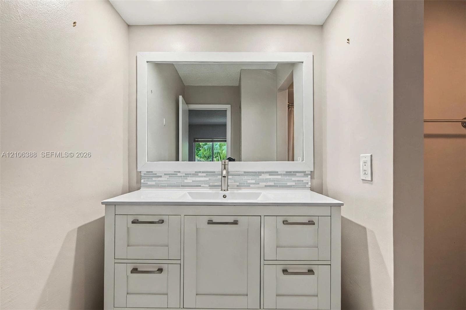 White cabinetry vanity featuring a rectangular integrated sink, white countertop, linear tile backsplash, and a framed mirror