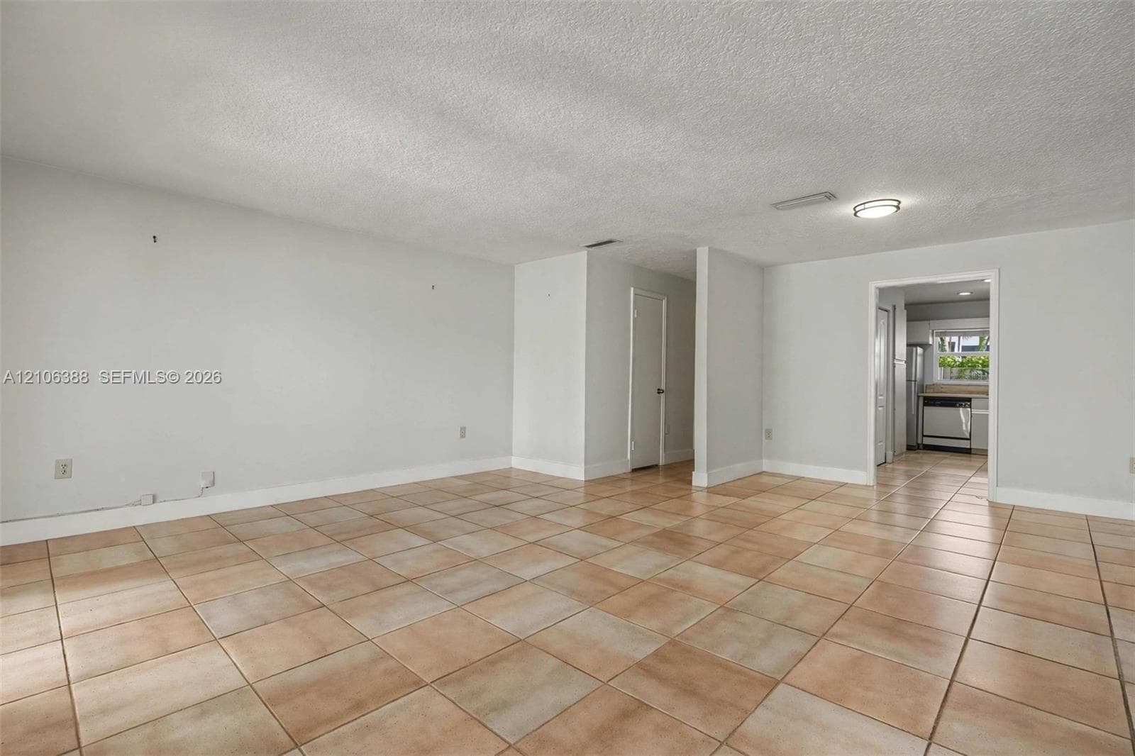 Neutral-toned interior space featuring light-colored ceramic tile flooring, a textured ceiling, and a flush-mount light fixture