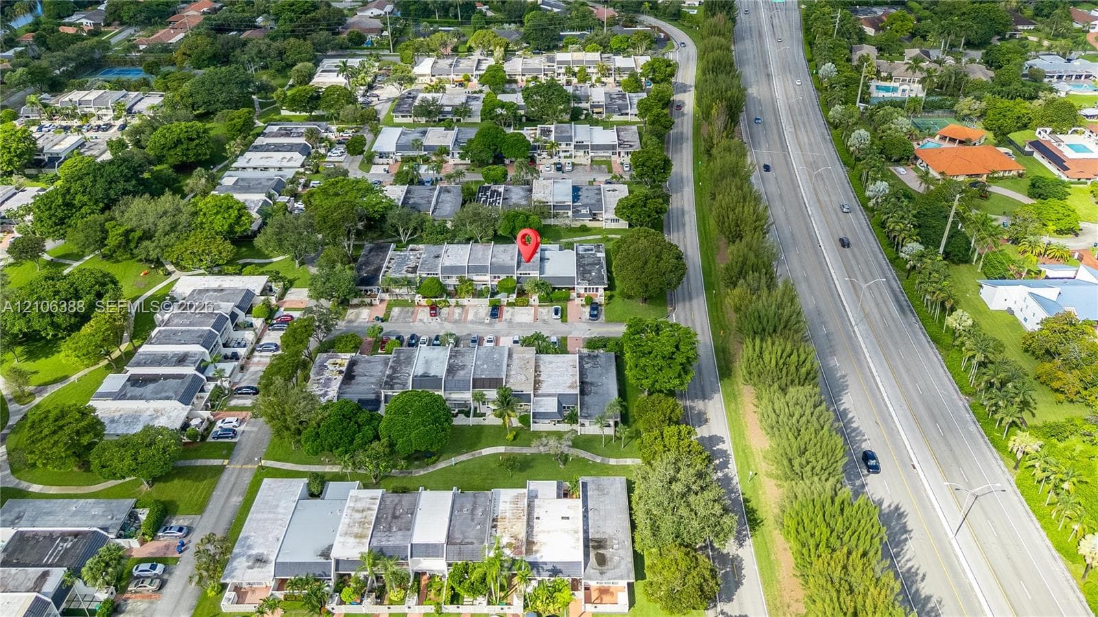 Aerial perspective featuring multi-unit residential structures, paved parking areas, and mature tree canopy throughout the grounds