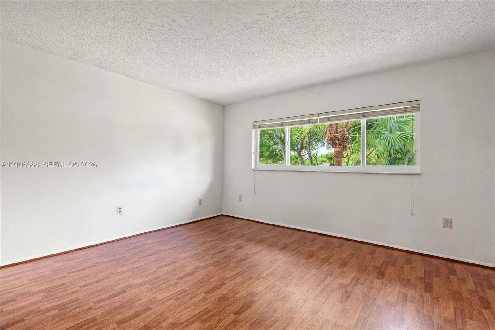 Room featuring wood-finish flooring, white walls, and a large horizontal window with blinds