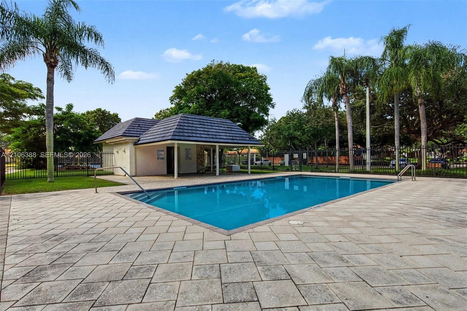 In-ground rectangular swimming pool featuring a tiled deck, metal handrails, and a nearby covered pavilion with a hipped roof