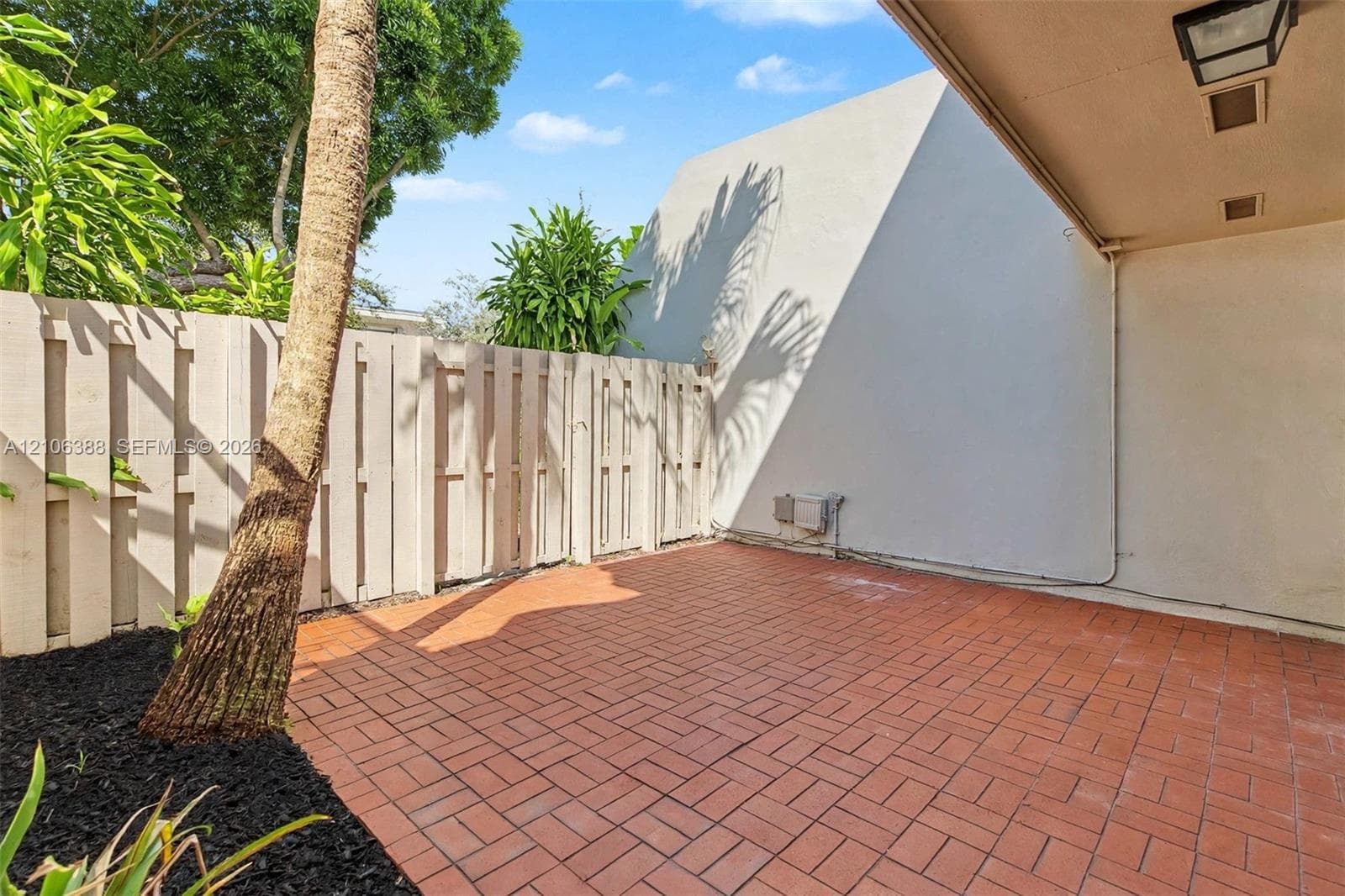 Private patio featuring red brick paving, a covered overhang with recessed lighting, and a solid wood privacy fence