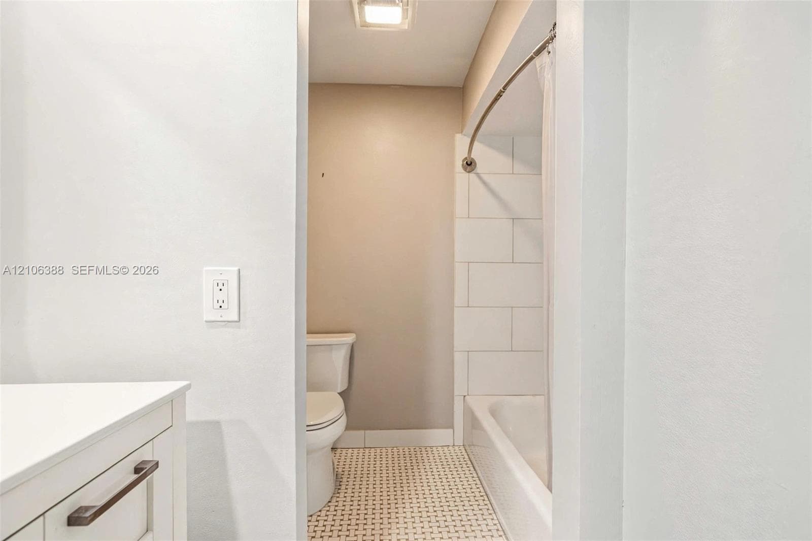 Bathroom featuring a white vanity, a tiled bathtub surround, a curved shower rod, and patterned tile flooring