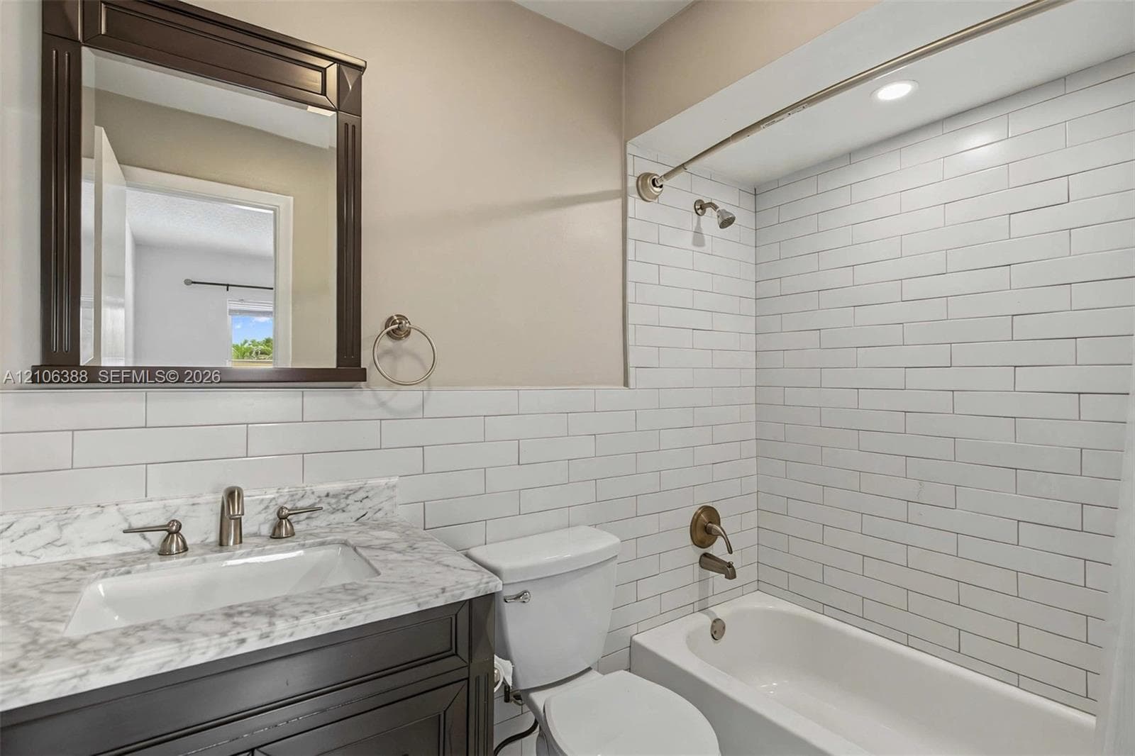 Bathroom featuring a dark wood vanity with a stone-finish countertop, undermount sink, white subway tile shower surround, and a framed mirror