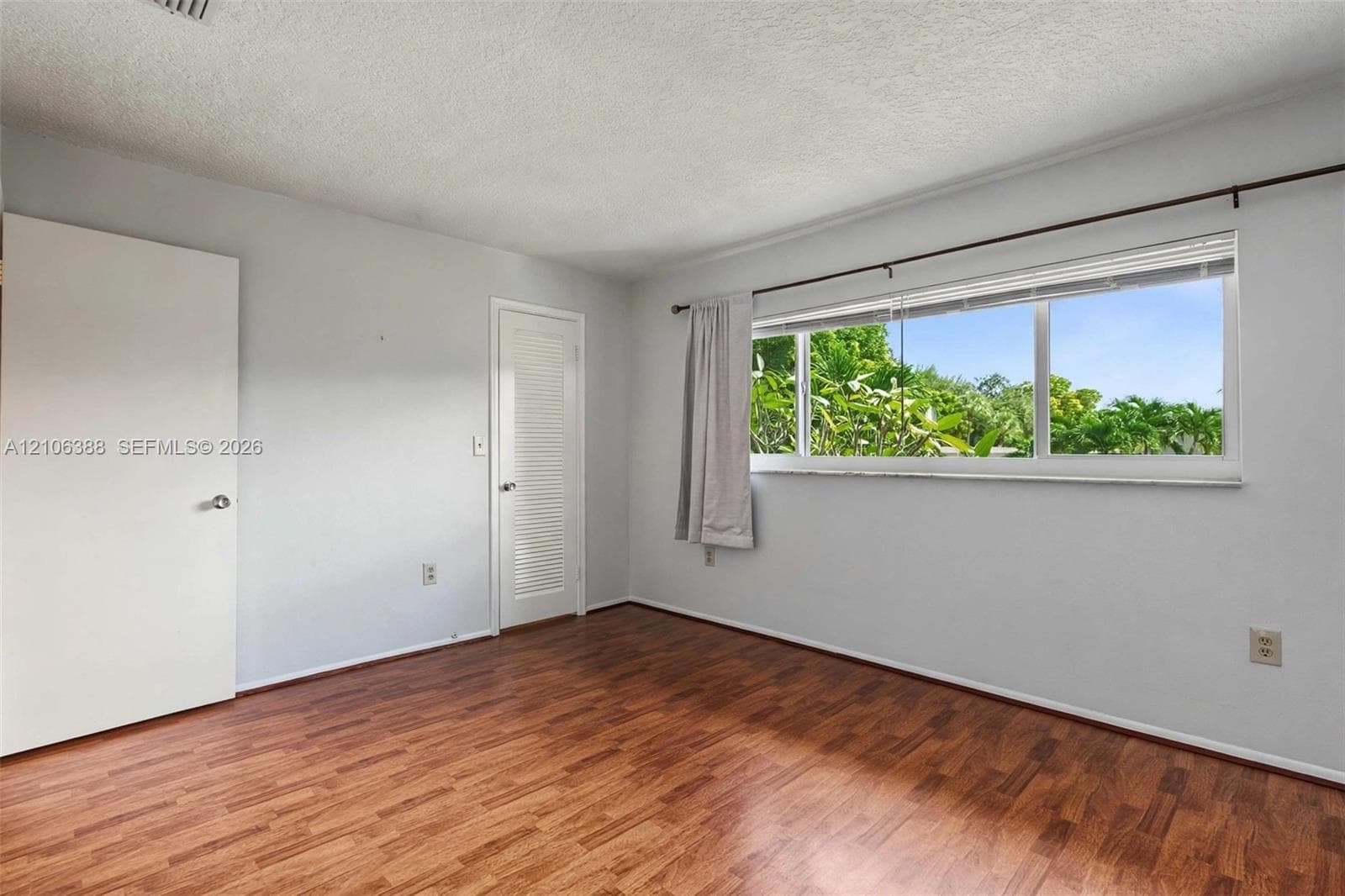 Room featuring wood-finish flooring, a large horizontal window with exterior foliage, and louvered closet door