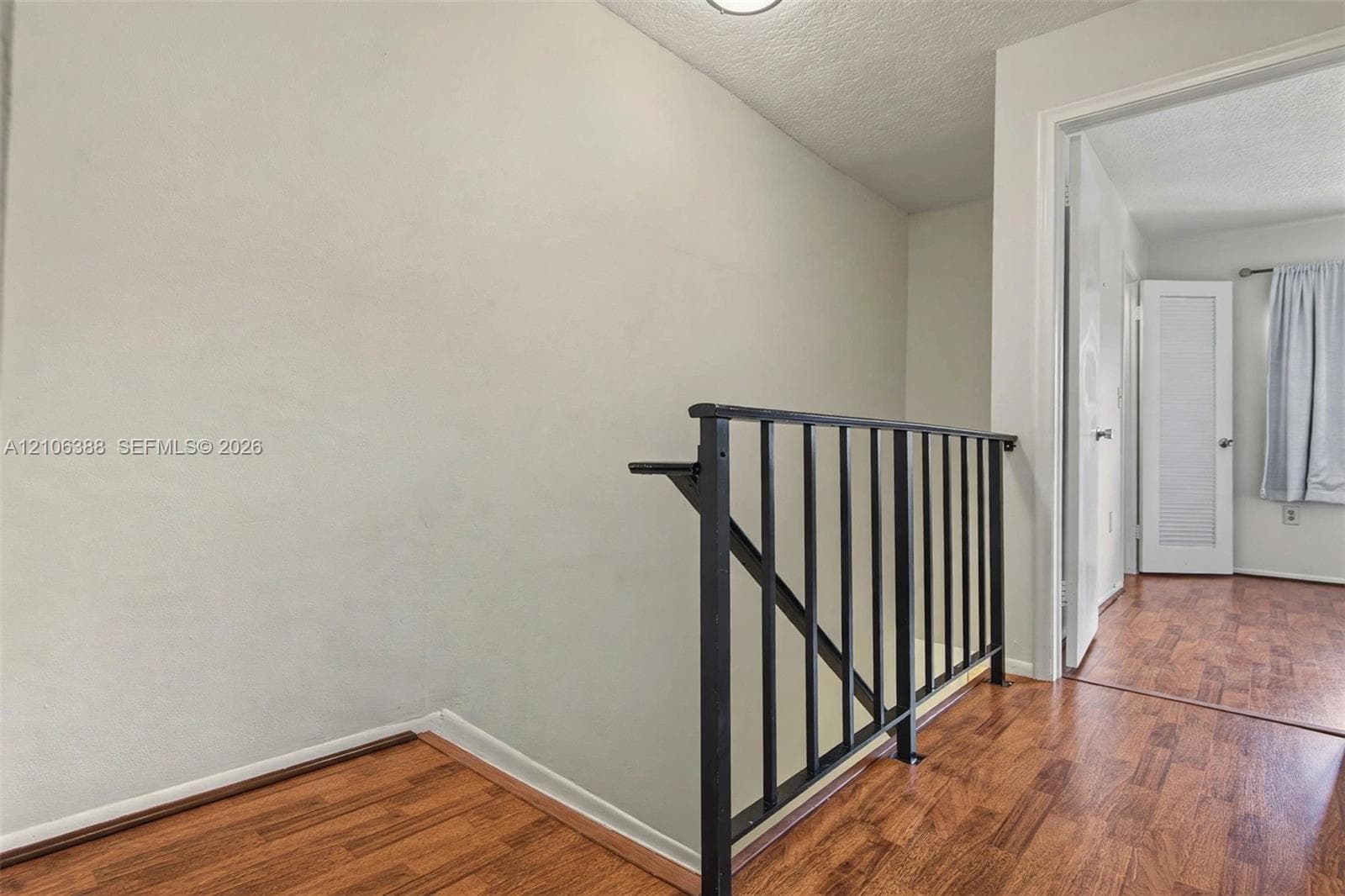 Wood-finish flooring featuring a black metal balustrade and a louvered panel door
