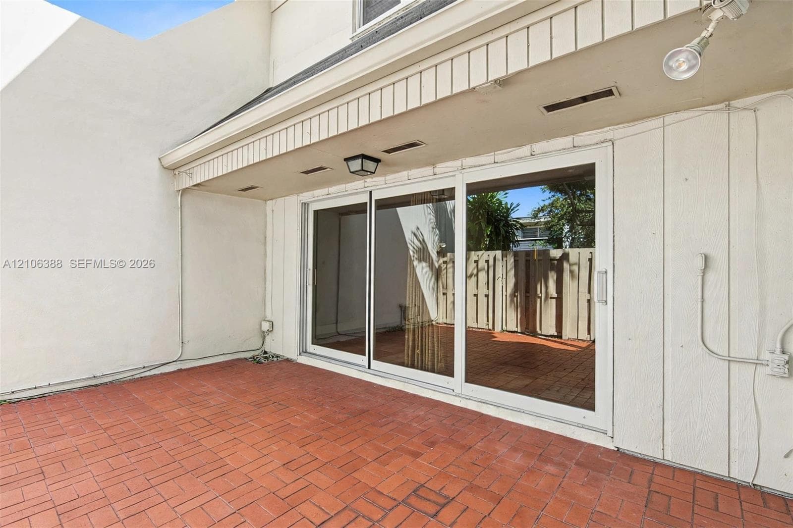 Private patio featuring red brick paving, a three-panel sliding glass door, and a covered entryway with integrated lighting