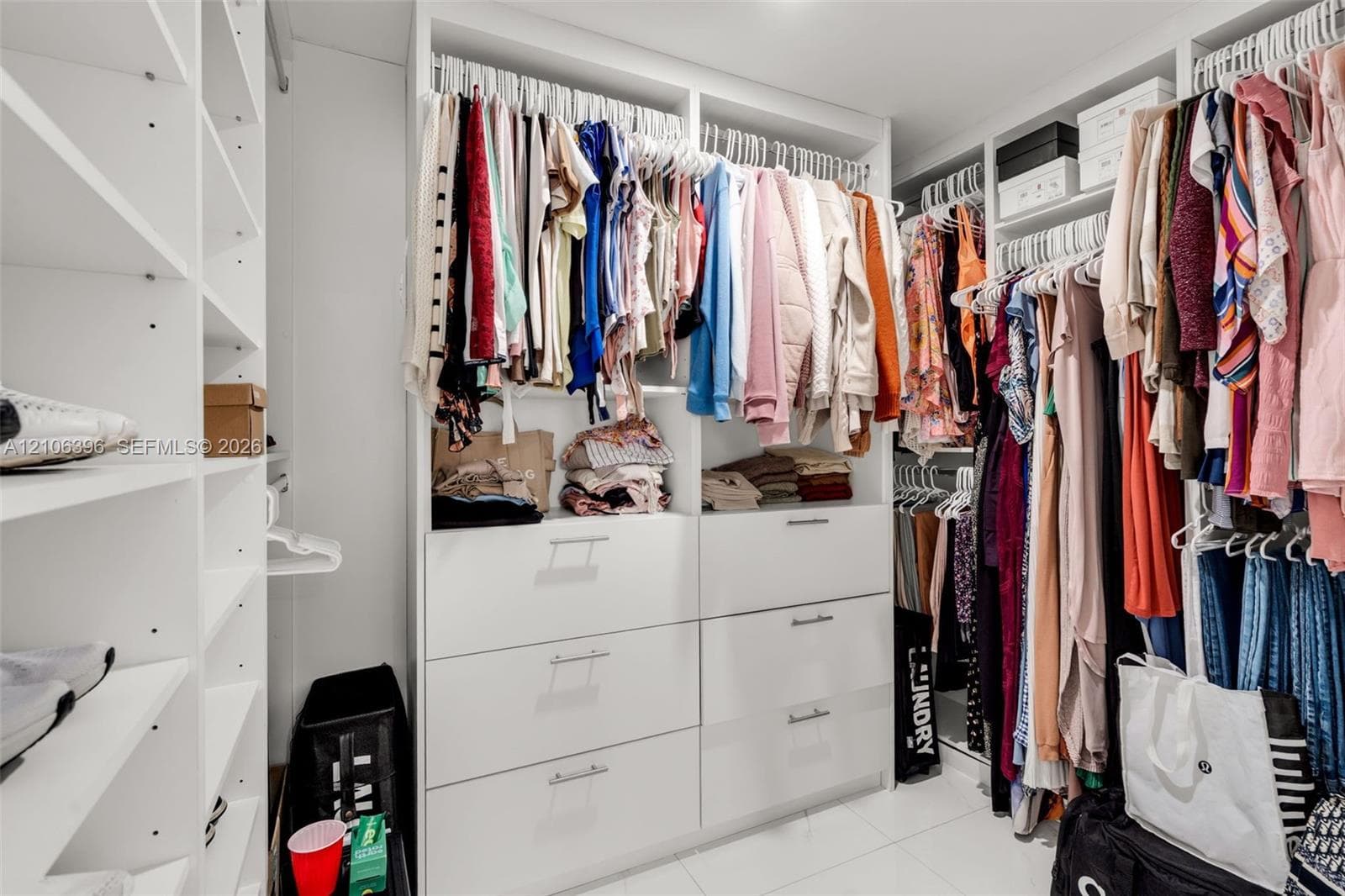 Custom walk-in closet featuring white built-in shelving, floor-to-ceiling storage, tiered hanging rods, and integrated soft-close drawer units with metallic hardware