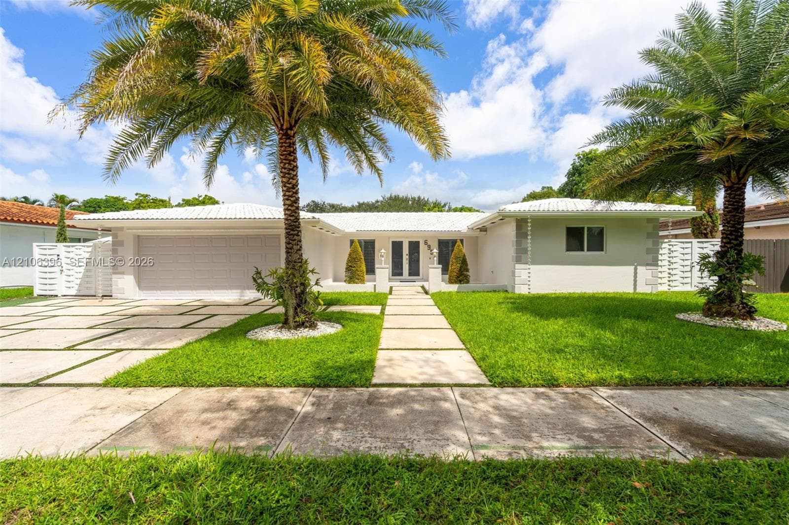 Single-story exterior featuring a light-toned facade, decorative corner quoins, a crisp white tile roof, an integrated garage, and a geometric paver driveway