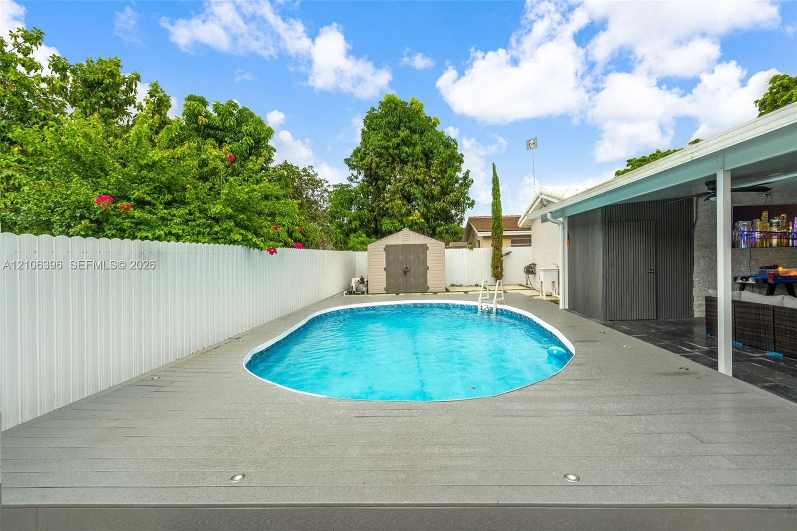 Outdoor area featuring an in-ground swimming pool, gray composite decking, white vinyl perimeter fencing, and a detached storage shed