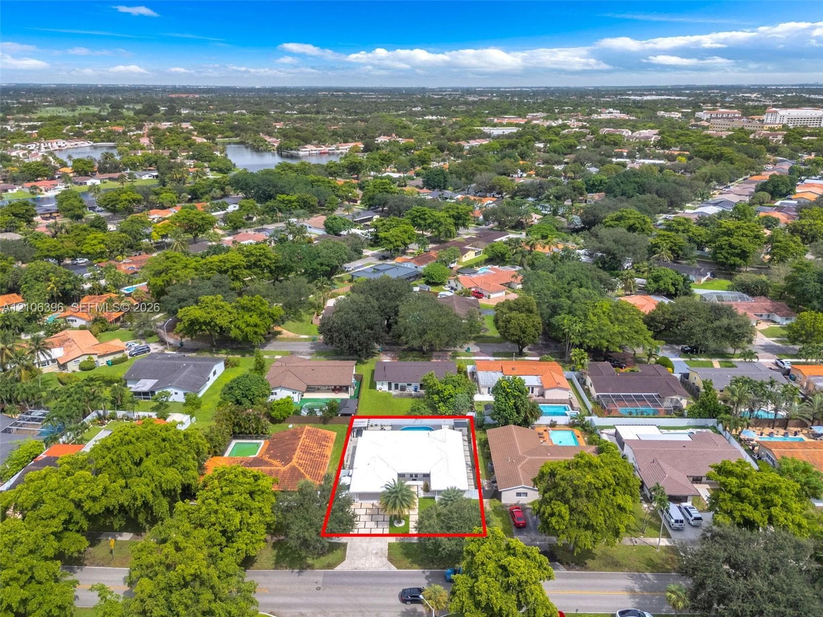 Aerial perspective of a property featuring a white-roofed structure, a backyard swimming pool, and a paved driveway