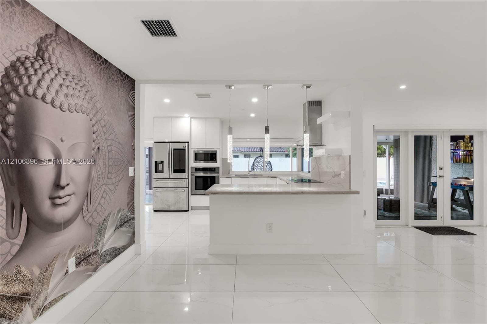 Kitchen featuring high-gloss cabinetry, stainless steel appliances, a peninsula with stone-finish countertops, three glass pendant lights, and large-format porcelain tile flooring