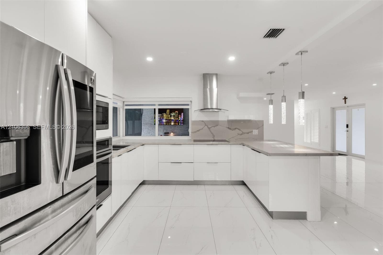 Kitchen featuring glossy white flat-panel cabinetry, stainless steel appliances, a peninsula with stone-finish countertops, full-height stone-finish backsplash, and three cylindrical pendant lights