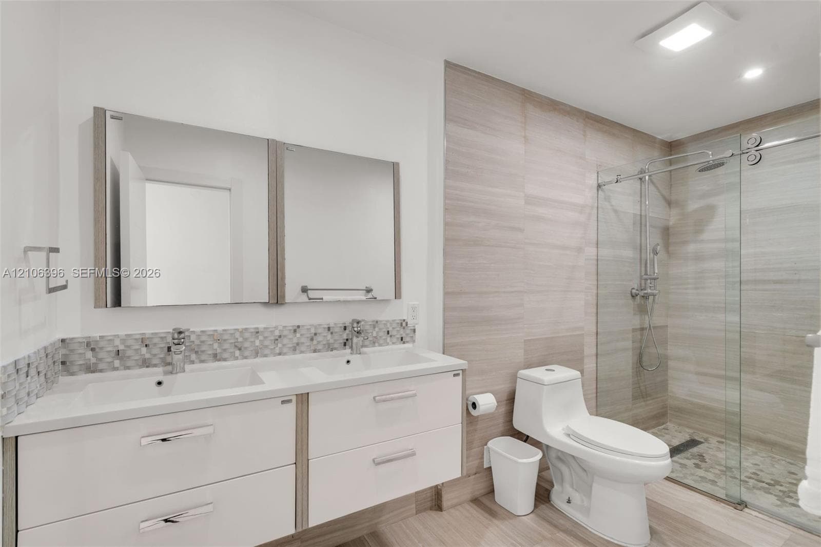Floating double vanity featuring white cabinetry, integrated sinks, and mosaic tile backsplash, paired with a glass-enclosed shower with horizontal tile surround, rain shower head, and pebble-tile flooring