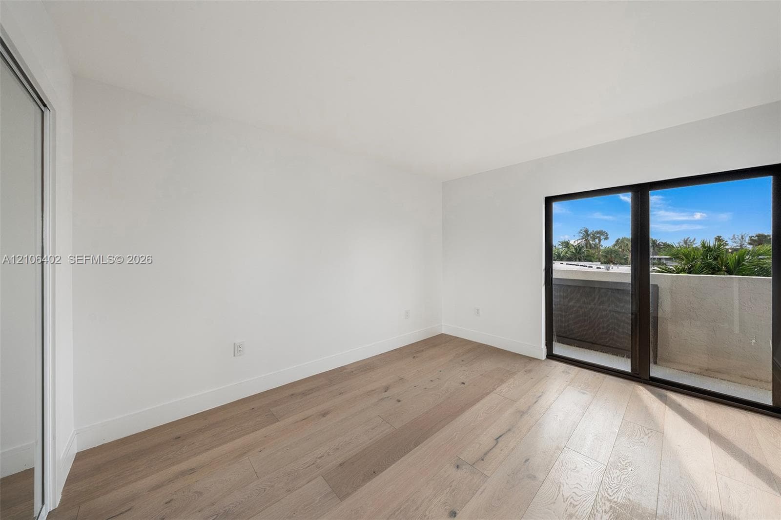 Neutral-toned interior featuring wood-finish flooring, sliding glass balcony doors with dark frames, and a mirrored closet door