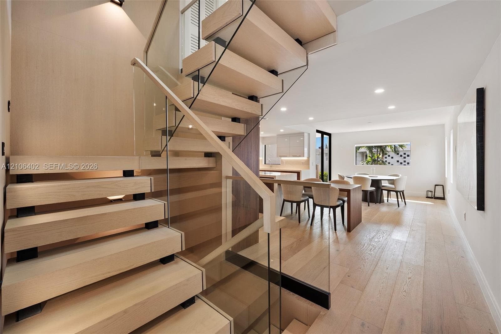 Floating staircase with wood treads, glass panel railings, recessed ceiling lighting, and wide-plank wood-finish flooring