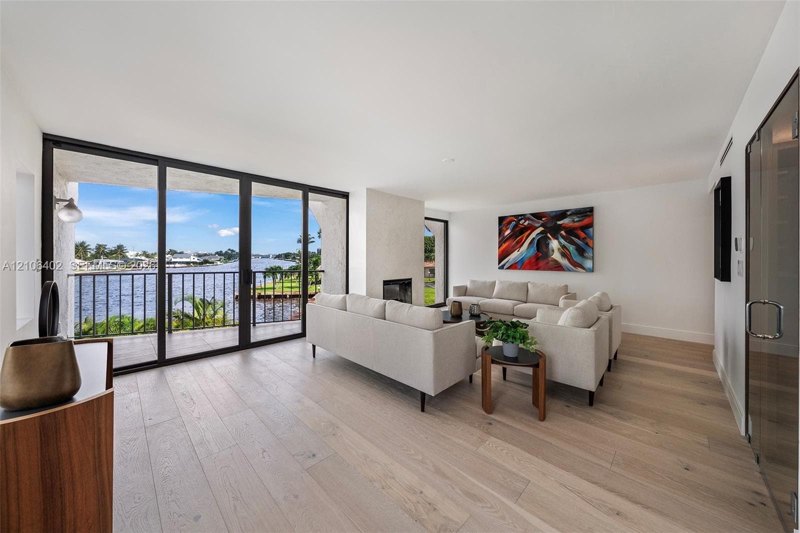 Living area featuring floor-to-ceiling glass sliding doors, wood-finish flooring, a built-in fireplace, and a balcony with metal railings overlooking the water