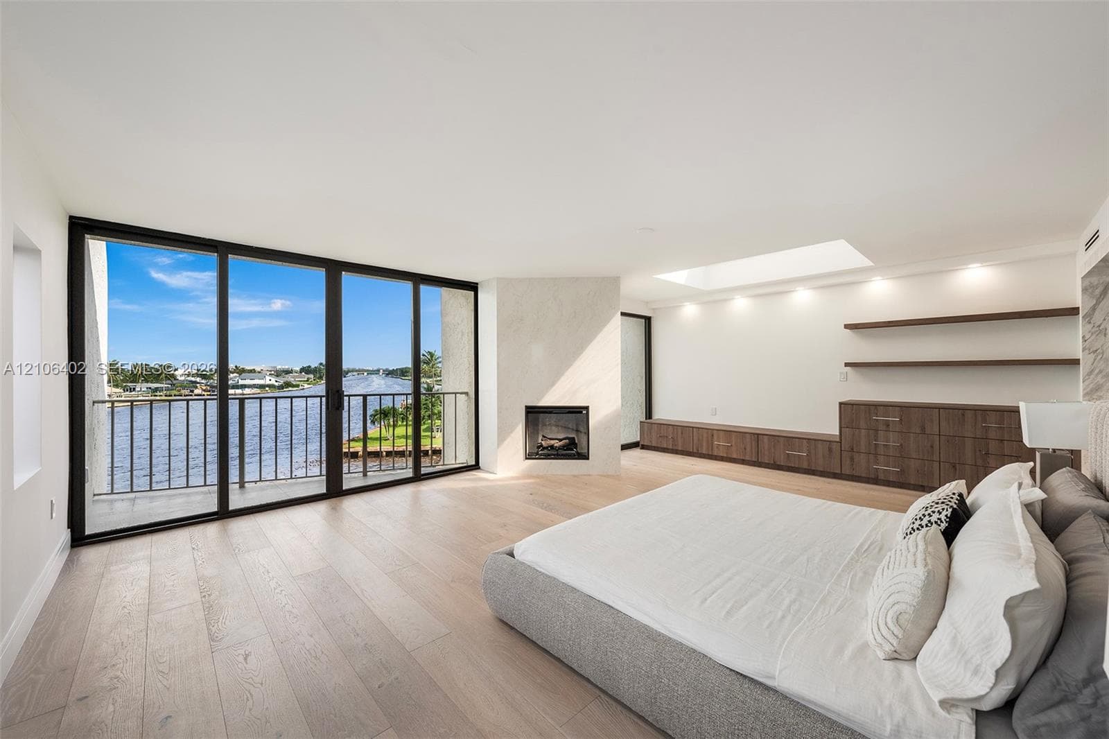 Floor-to-ceiling sliding glass doors, built-in wooden cabinetry with matching wall-mounted shelving, integrated fireplace with a neutral surround, recessed ceiling lighting, and overhead skylight