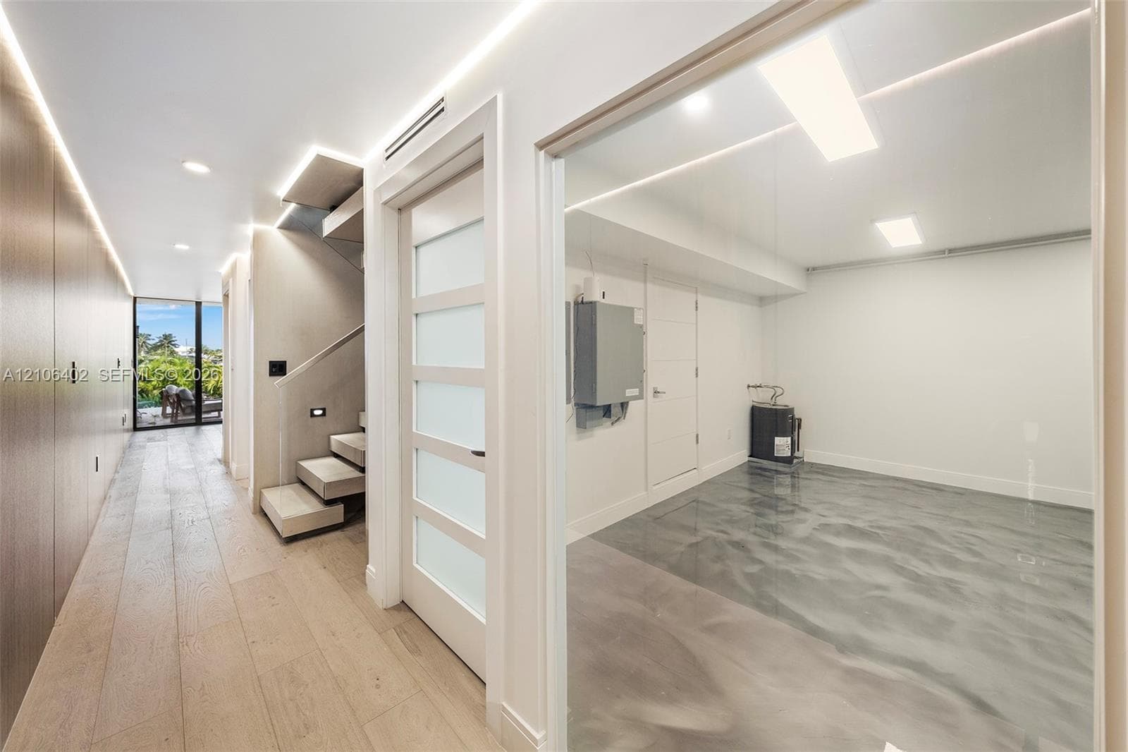 Interior space featuring wood-finish flooring, floating staircase with integrated lighting, frosted glass panel door, and epoxy floor finish in the enclosed room