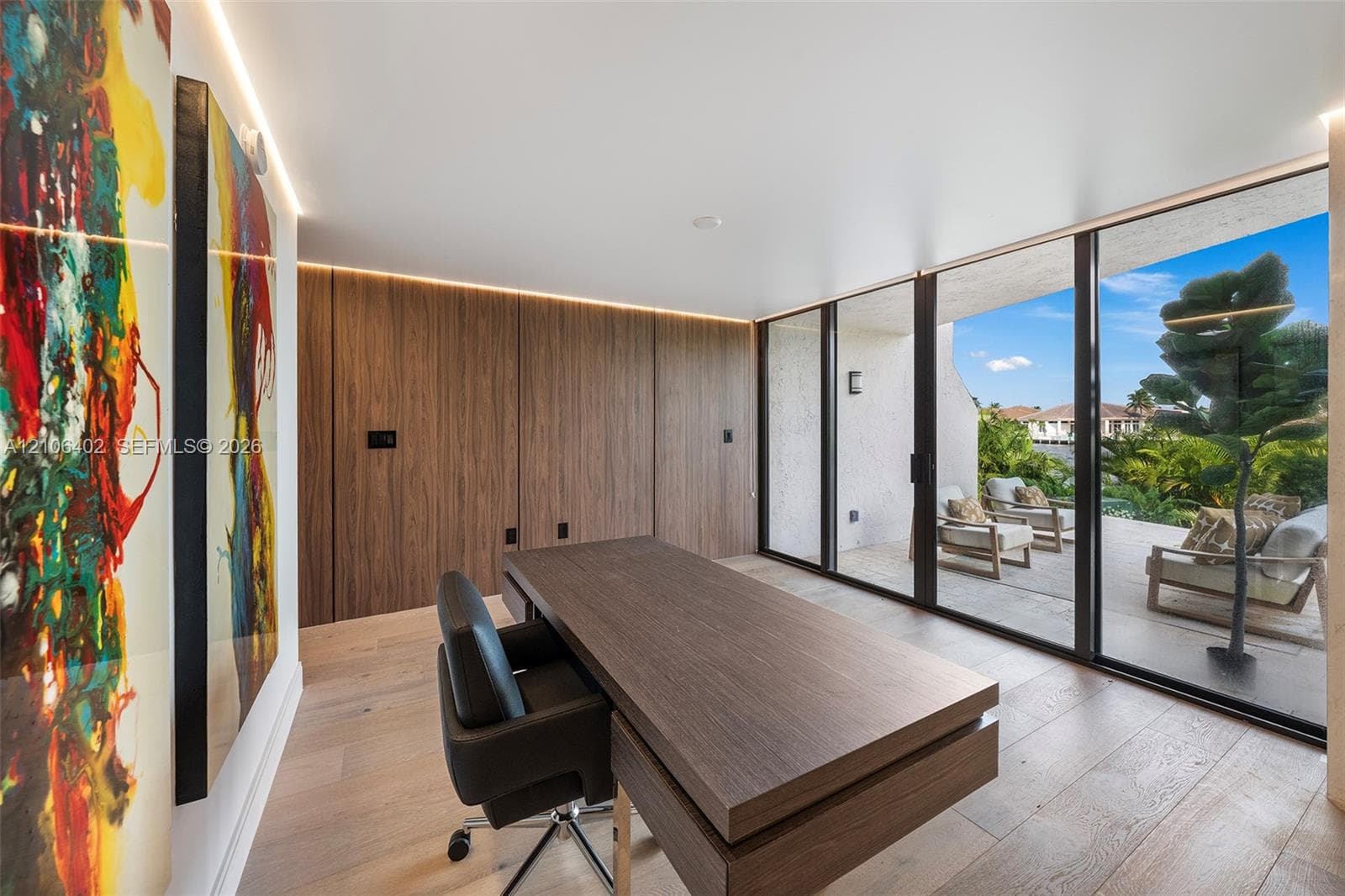 Floor-to-ceiling glass sliding doors, integrated wood-panel wall cabinetry, recessed perimeter lighting, and light-tone wood-finish flooring