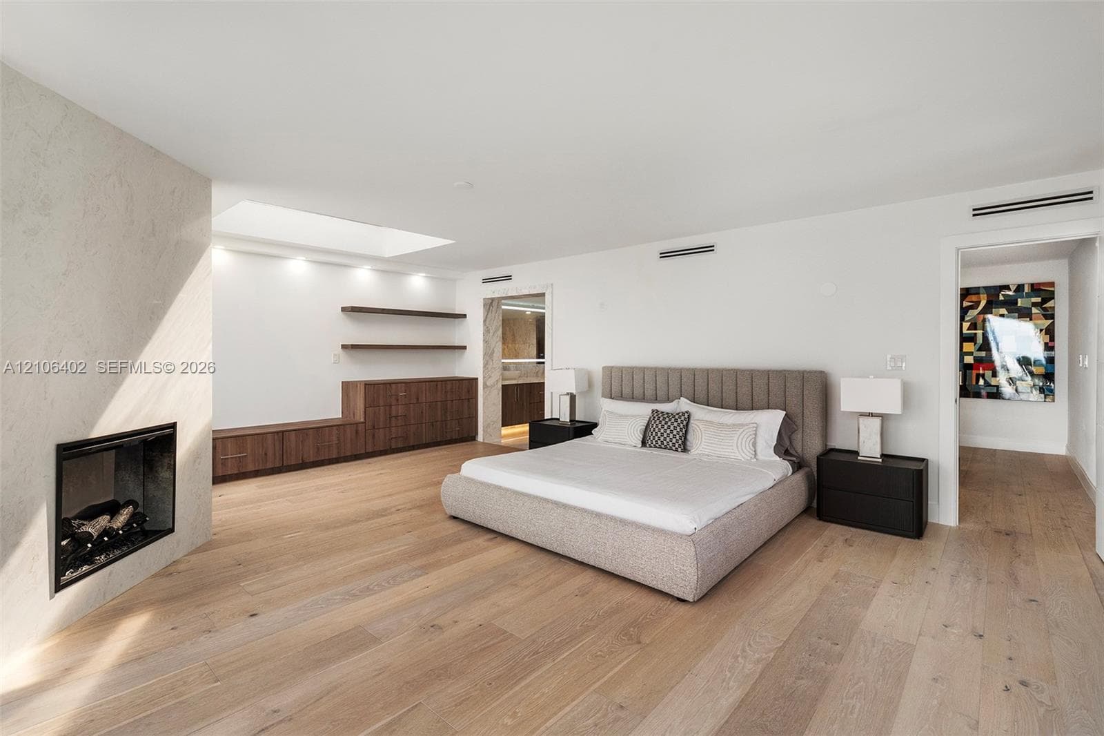 Open-concept room featuring light wood-finish flooring, a linear fireplace with a stone-surround, a skylight, and built-in wood cabinetry with floating shelves