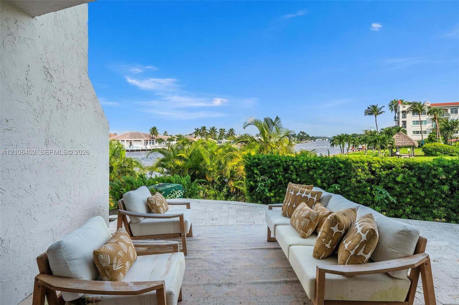 Covered stone-paved patio featuring expansive water frontage and mature perimeter landscaping