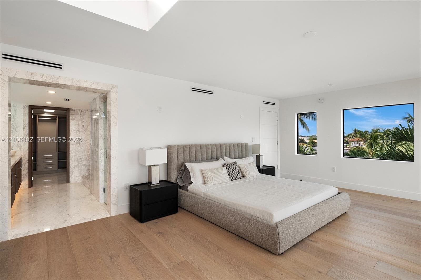 Light-filled room featuring wood-finish flooring, stone-surround entryway, skylight, and large-format windows with exterior landscape scenery