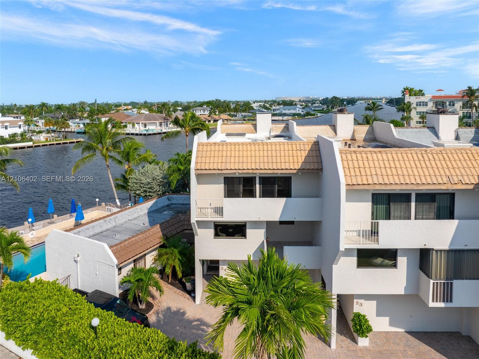 Waterfront townhome featuring a tile roof, paved driveway, private balconies, and proximity to a canal