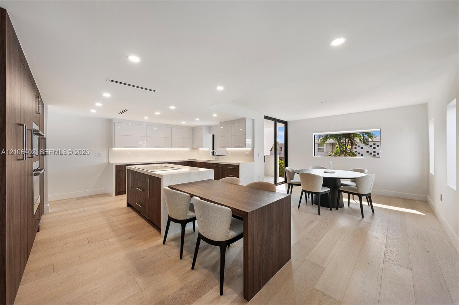 Kitchen featuring two-tone cabinetry, expansive center island with stone-finish countertops, built-in wall ovens, and wood-finish flooring