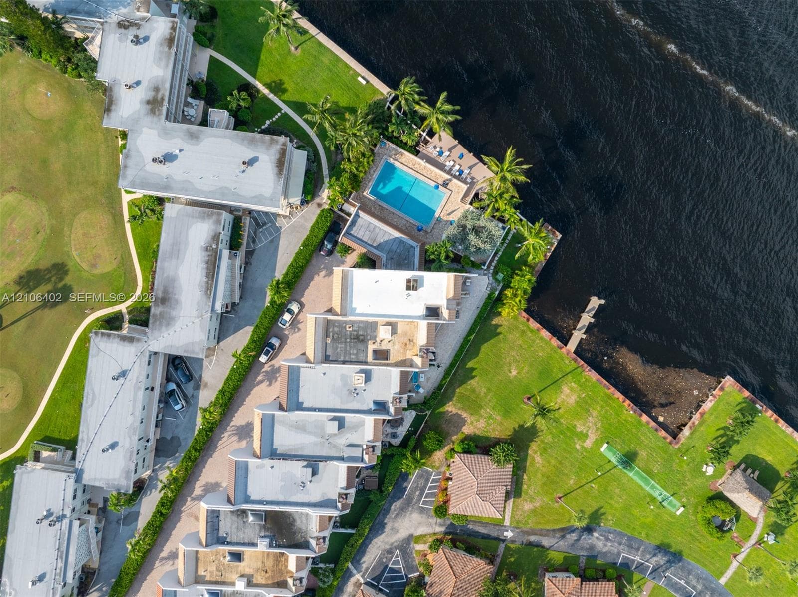 Aerial perspective of waterfront property featuring a swimming pool, paved patio, dock, and manicured green space