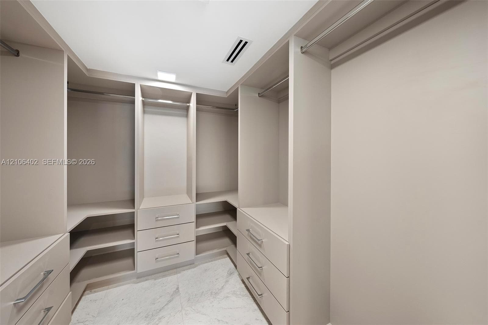 Walk-in closet featuring custom built-in cabinetry, floor-to-ceiling shelving, integrated drawer stacks, polished metal hardware, and large-format stone-finish flooring