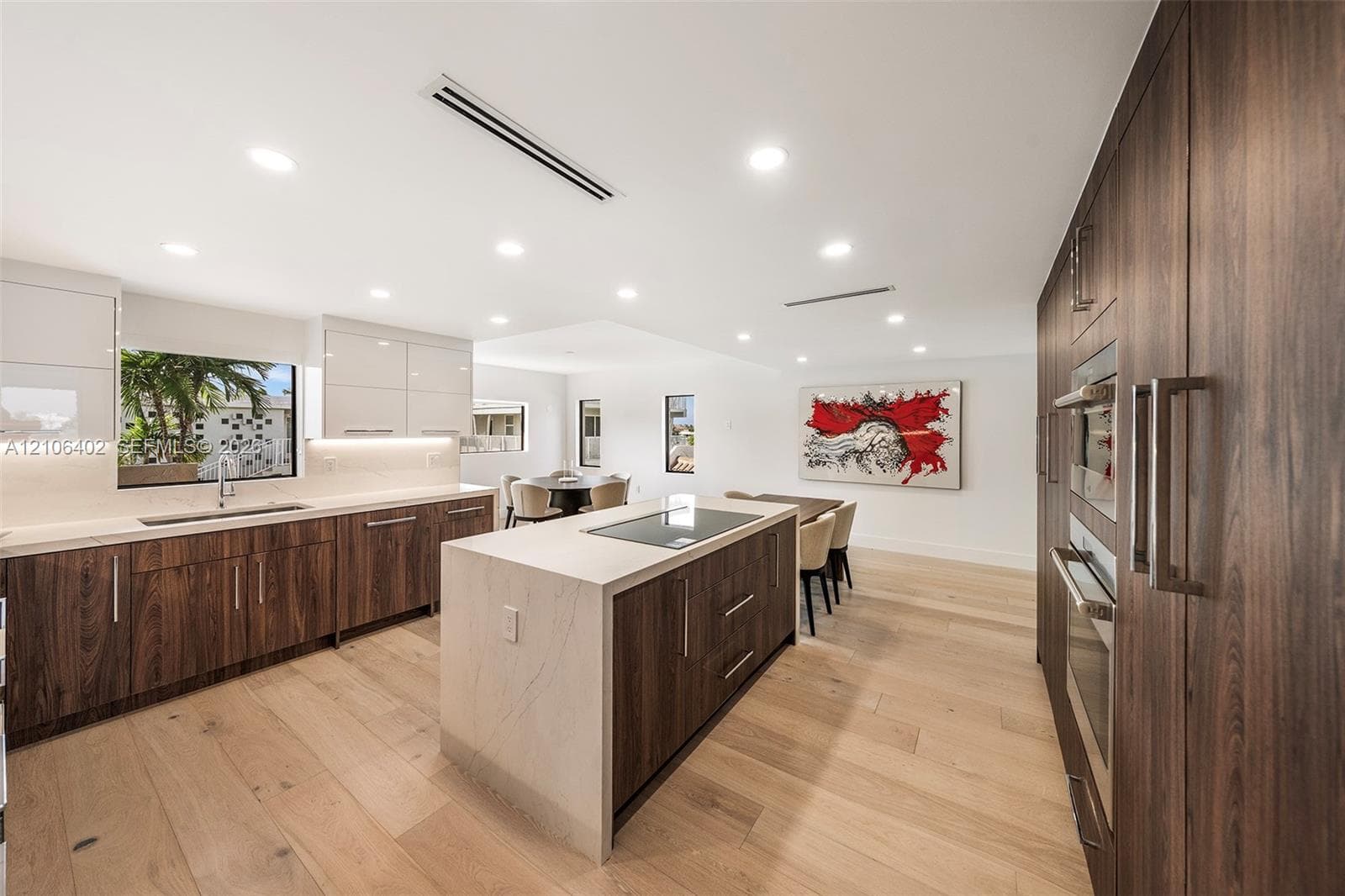Kitchen featuring high-gloss upper cabinetry, wood-finish lower cabinetry, stone-surface countertops, center island with an integrated cooktop, and wide-plank wood-finish flooring