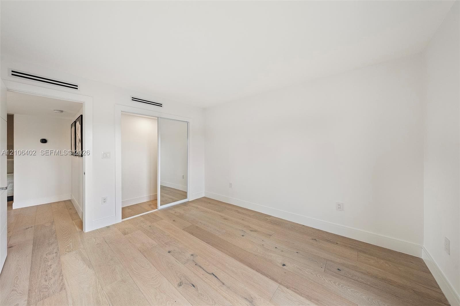 Neutral interior space featuring wood-finish flooring, recessed ceiling lighting, and a closet with sliding mirrored doors