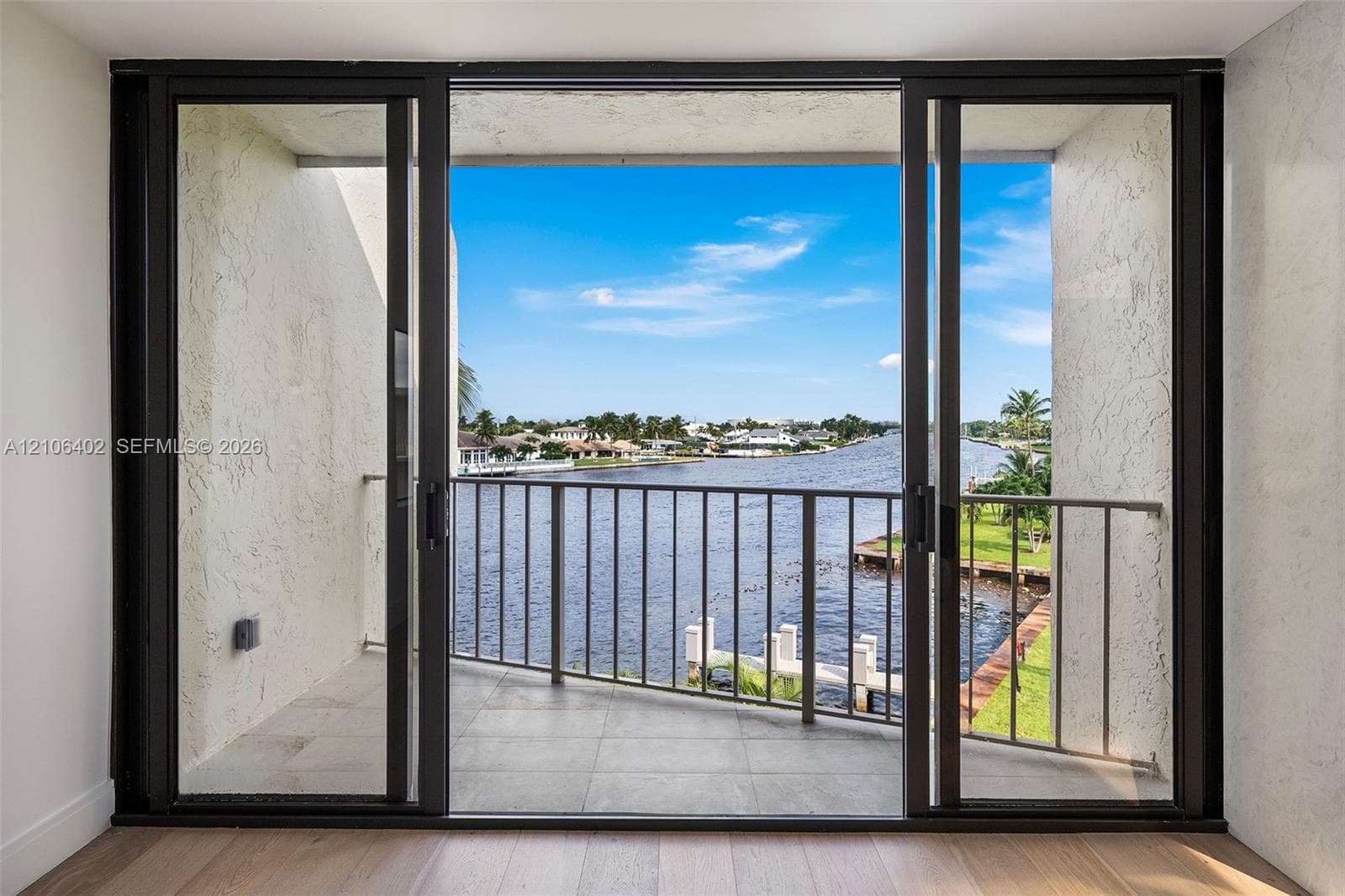 Large glass sliding doors opening to a balcony with metal railings, tile flooring, and water frontage
