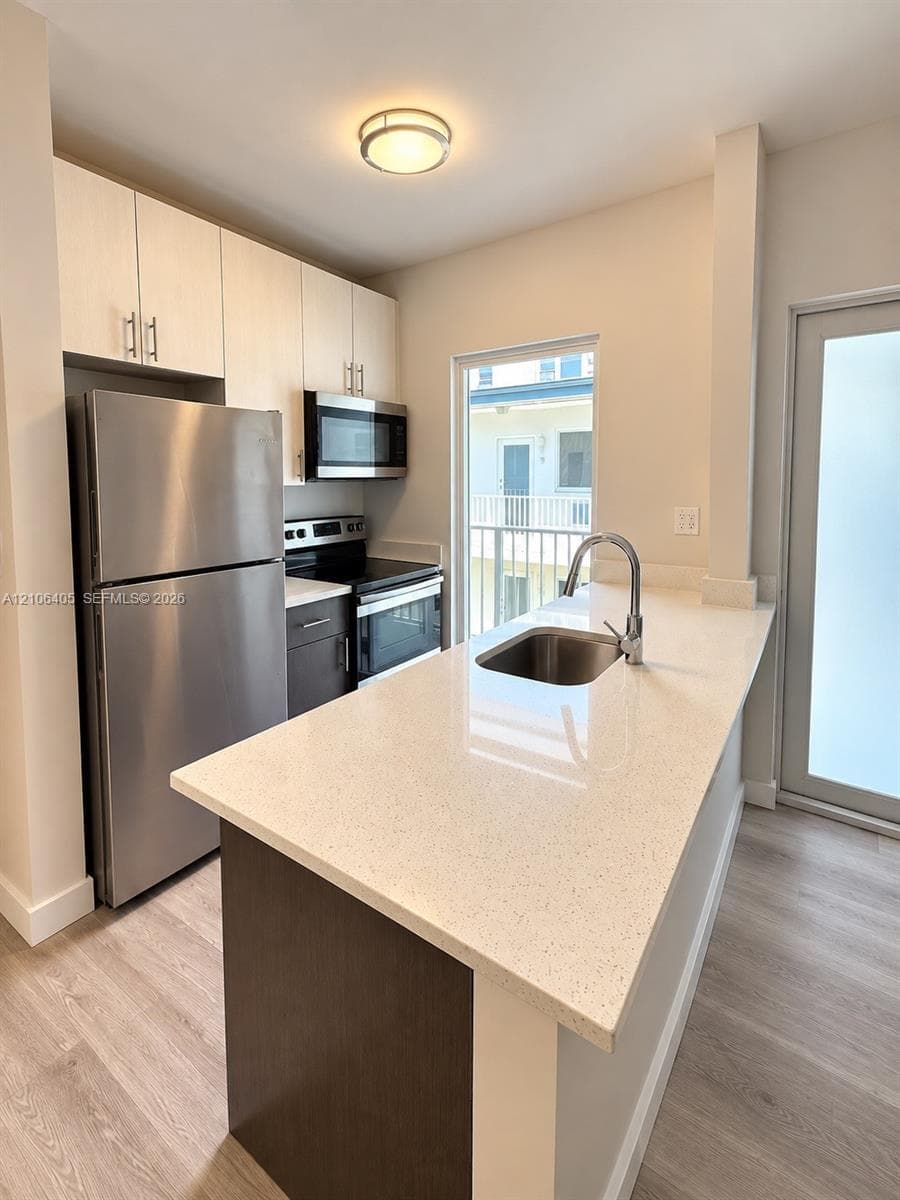 Kitchen featuring light-toned cabinetry, stainless steel appliances, quartz countertops, a stainless steel undermount sink with a gooseneck faucet, and wood-finish flooring