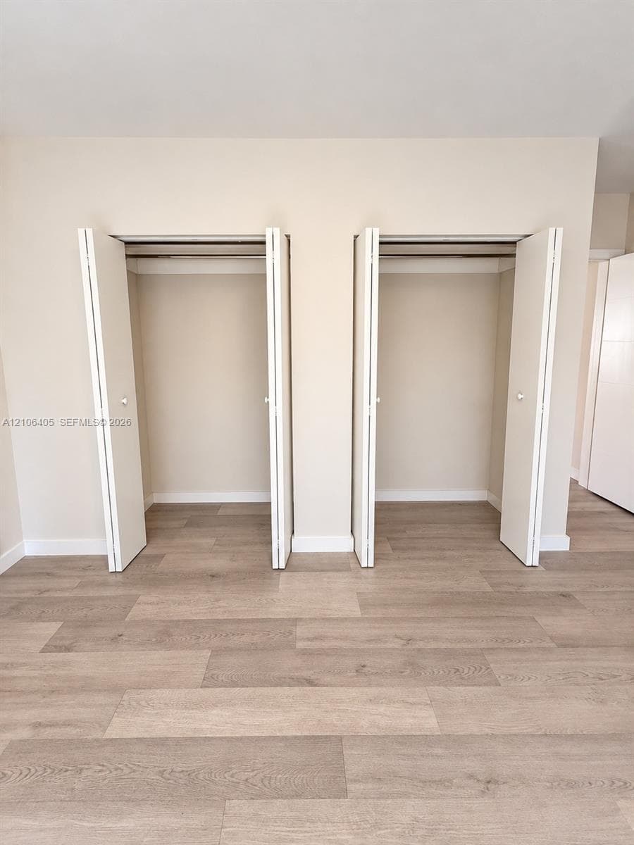 Dual reach-in closets featuring white bi-fold doors and wood-finish flooring