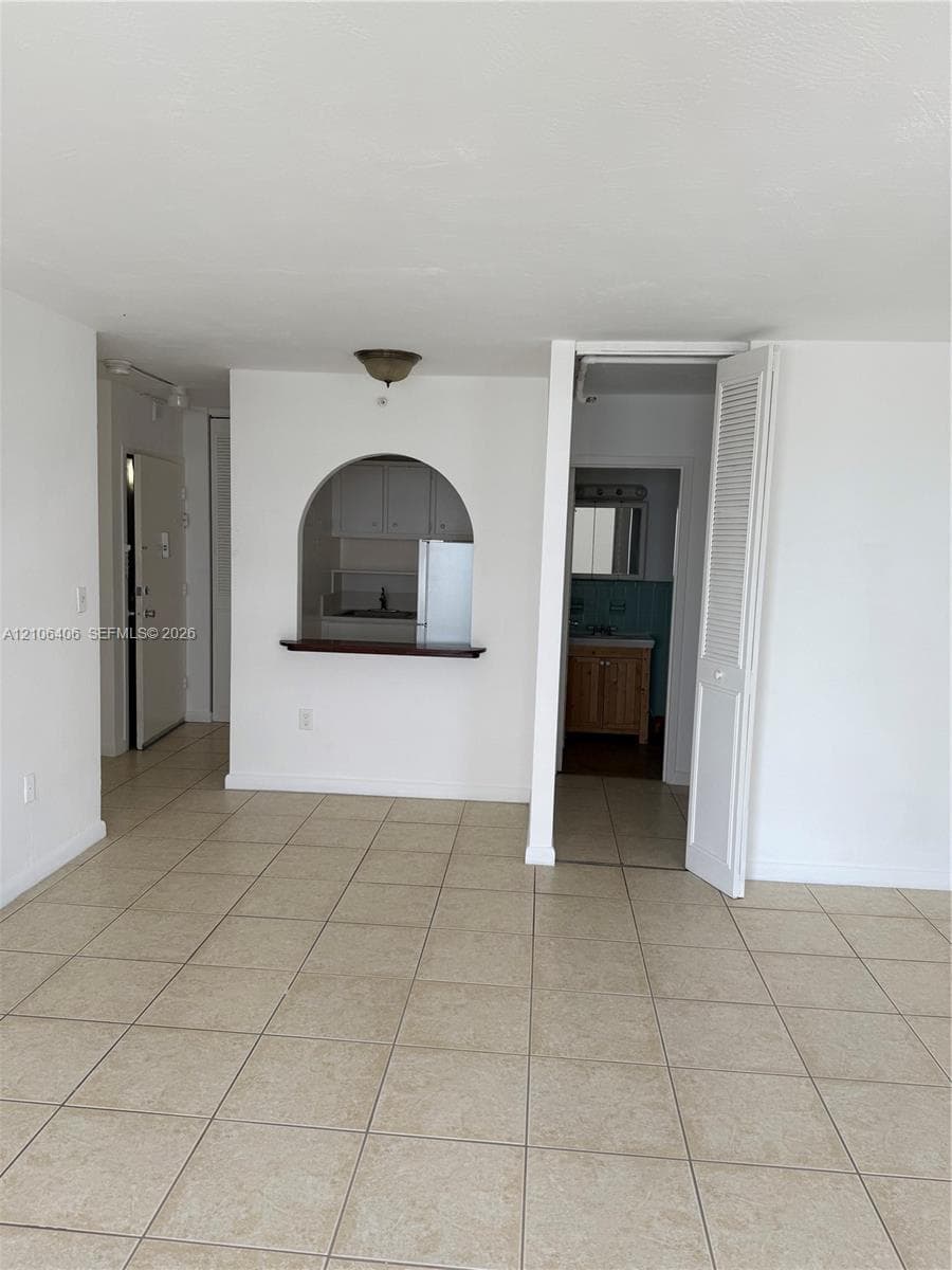 Neutral tile flooring, arched pass-through window with a built-in counter, and louvered closet door