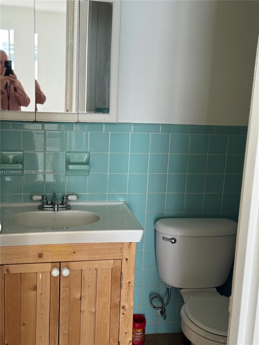 Bathroom featuring light wood cabinetry, a white porcelain sink with a chrome dual-handle faucet, a medicine cabinet, and blue square-tile backsplash with integrated soap dishes