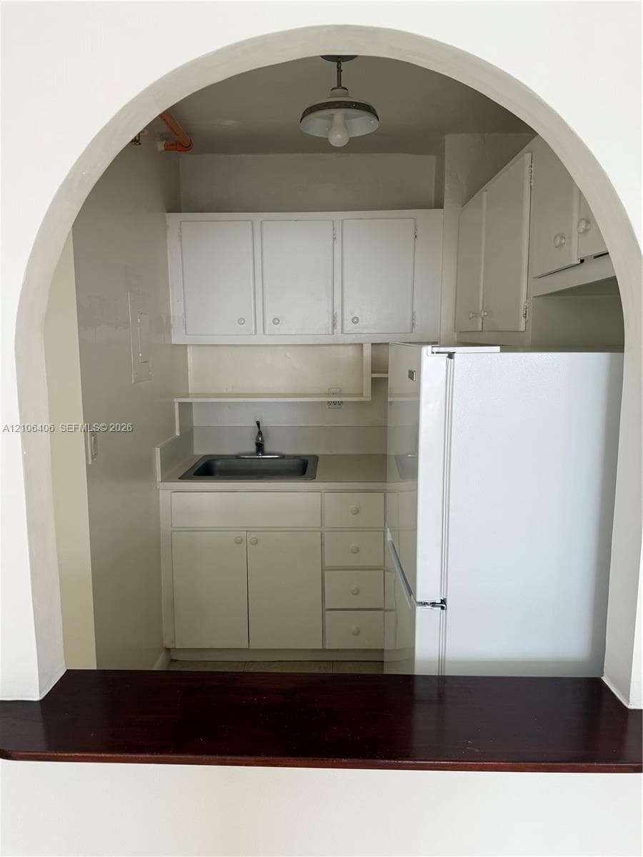 Arched entryway featuring a stained wood passthrough counter, white cabinetry, solid-surface countertops, single-basin drop-in sink, and pendant lighting