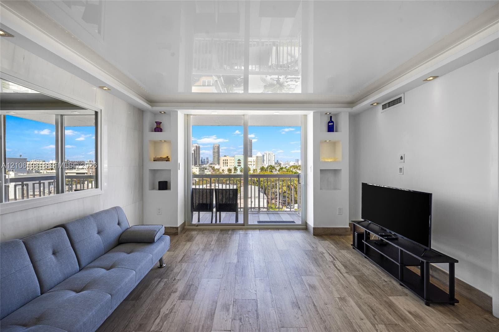 High-gloss ceiling, wood-finish flooring, built-in shelving with recessed accent lighting, and large sliding glass doors opening to a balcony