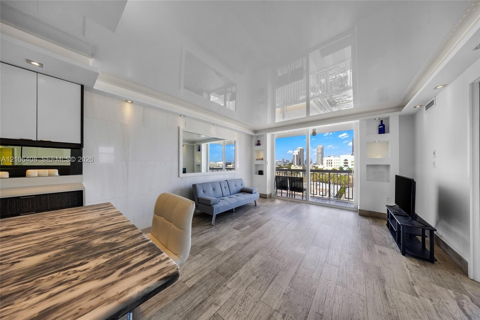 Living area featuring a high-gloss reflective ceiling, wood-finish flooring, built-in shelving, and floor-to-ceiling glass sliding doors opening to a balcony