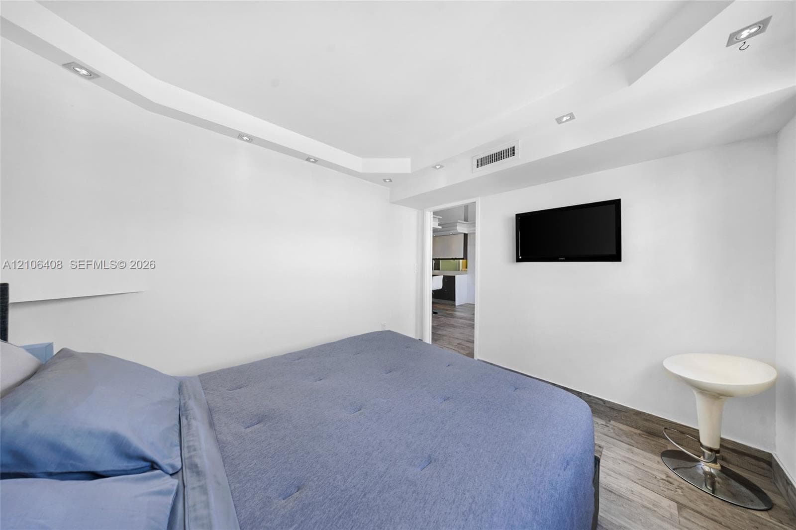 Tray ceiling with integrated recessed lighting, wood-finish flooring, and wall-mounted television