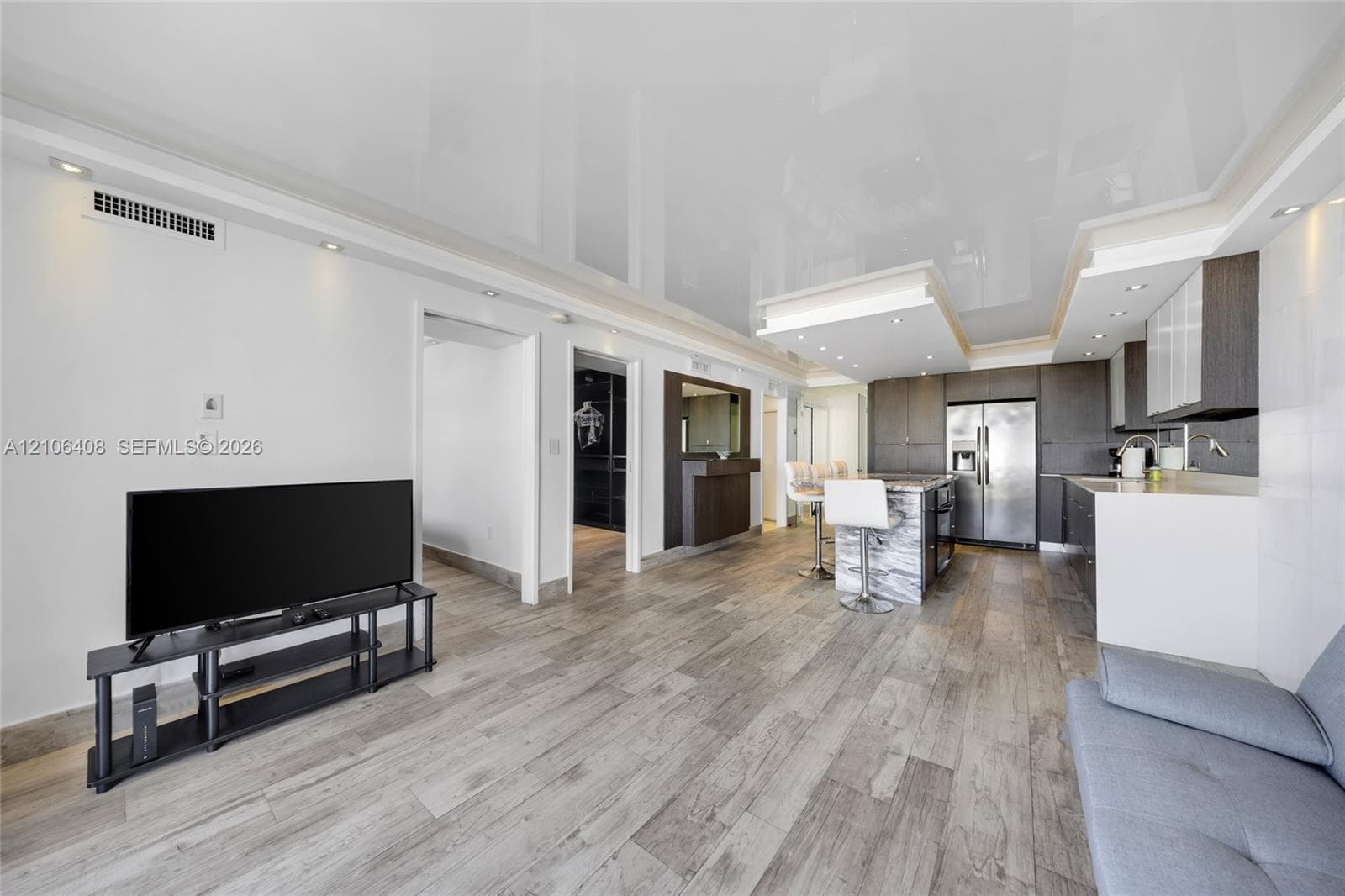 Open-concept space featuring a high-gloss ceiling, wood-finish flooring, recessed lighting, built-in cabinetry, and a kitchen island with a stone-finish facade