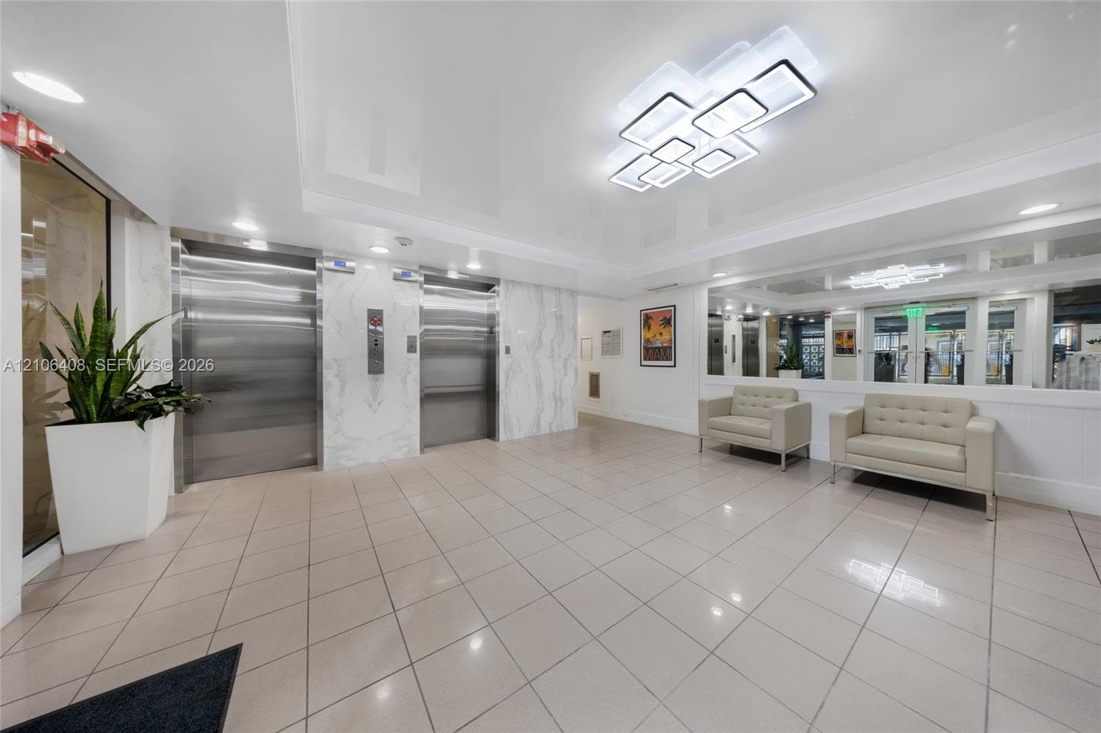 Lobby featuring dual stainless steel elevators, polished stone-finish wall cladding, large-format tile flooring, reflective wall-to-wall mirror panels, and contemporary geometric ceiling lighting