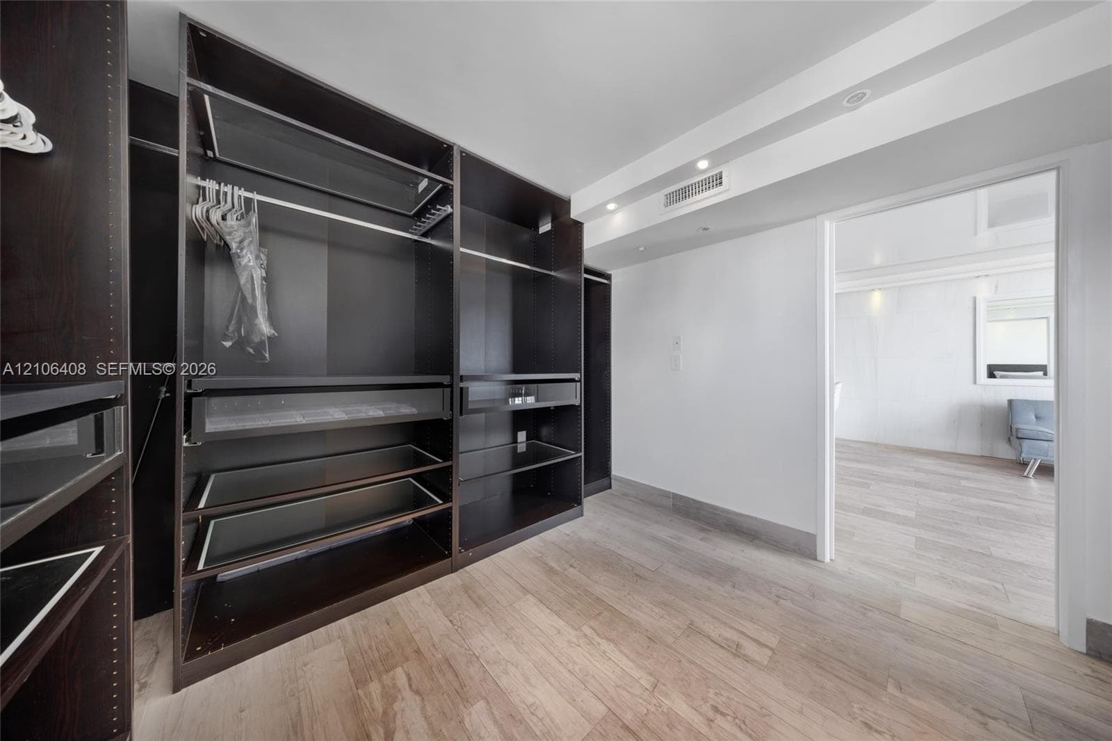 Walk-in closet featuring custom dark-finish floor-to-ceiling cabinetry, integrated shelving units, recessed ceiling lighting, and wood-finish flooring